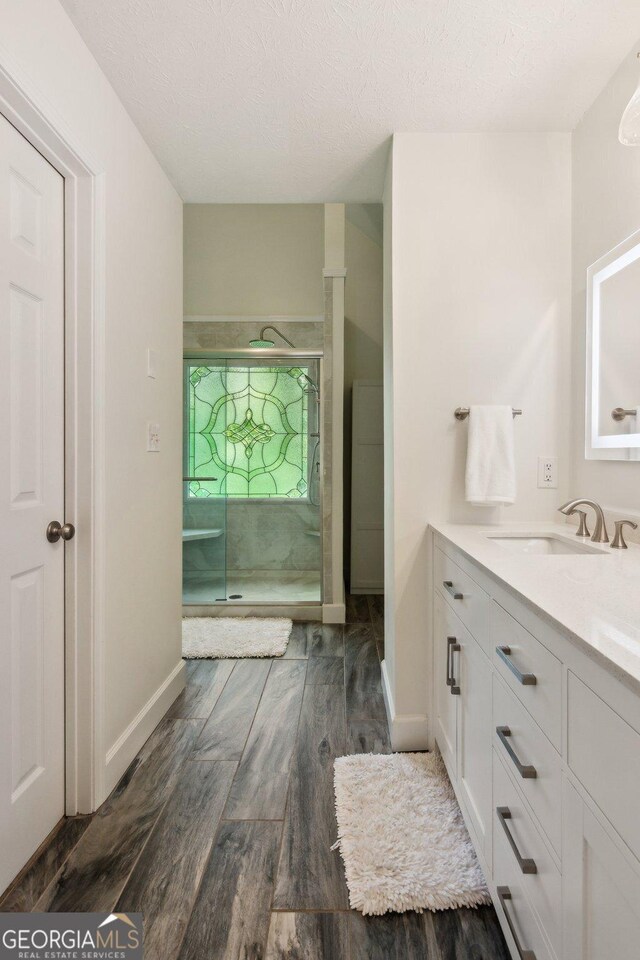 full bath with vanity, baseboards, wood finished floors, and a stall shower
