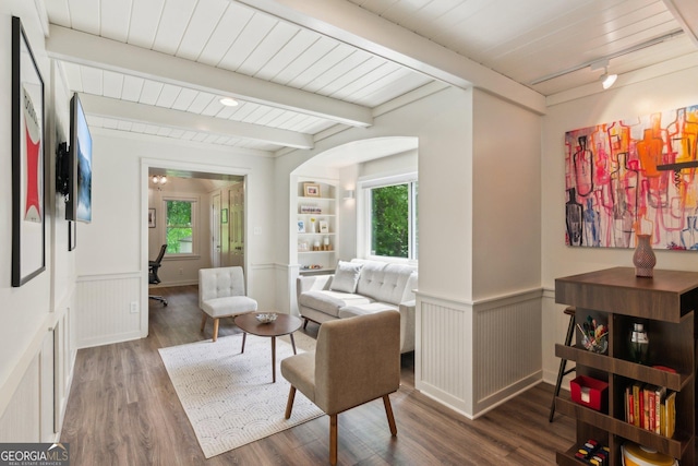 living area featuring wood finished floors, beam ceiling, wainscoting, arched walkways, and wooden ceiling