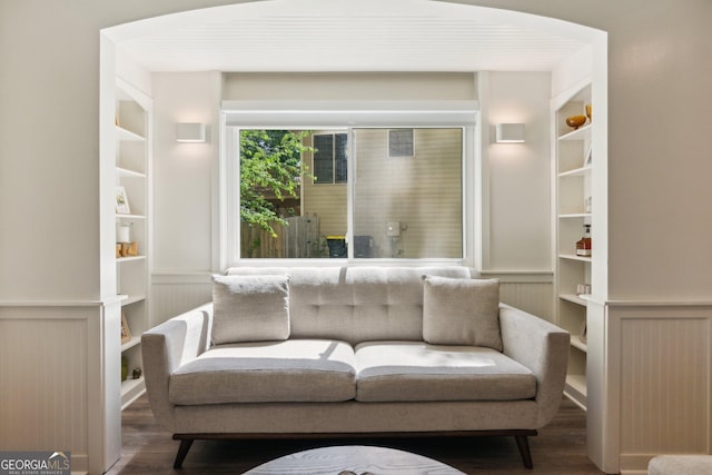 living area featuring a decorative wall, wood finished floors, built in shelves, and wainscoting