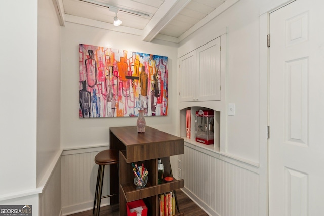 hall featuring a decorative wall, a wainscoted wall, beam ceiling, dark wood-type flooring, and track lighting