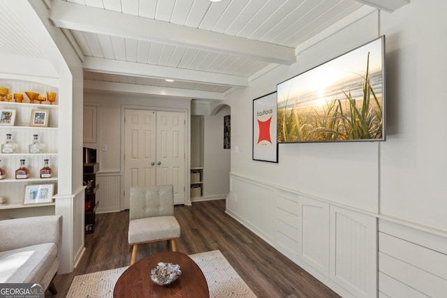 sitting room featuring a wainscoted wall, dark wood-type flooring, beamed ceiling, arched walkways, and wood ceiling