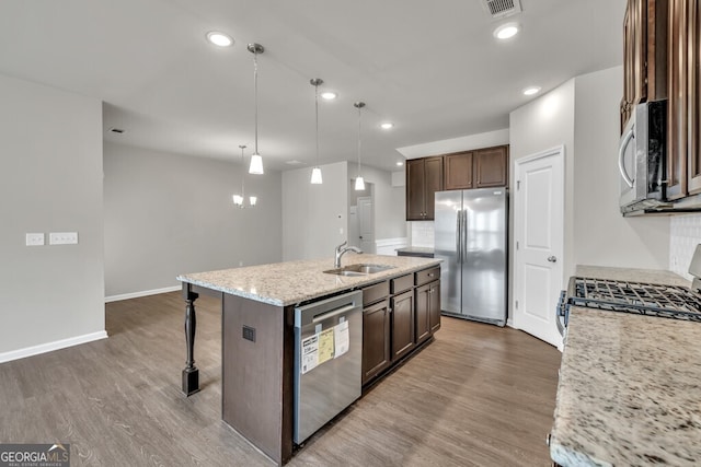 kitchen with stainless steel appliances, a sink, a kitchen island with sink, a kitchen bar, and dark brown cabinetry