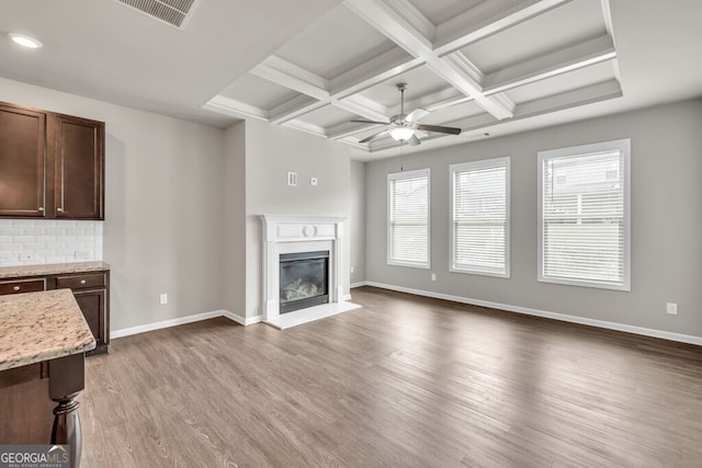unfurnished living room featuring ceiling fan, wood finished floors, beamed ceiling, a glass covered fireplace, and baseboards