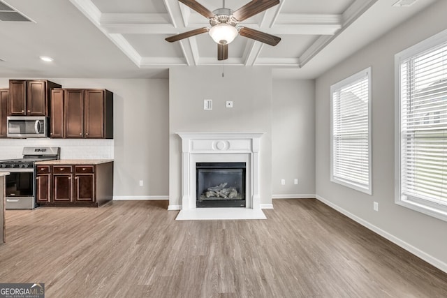 unfurnished living room featuring coffered ceiling, light wood-type flooring, ceiling fan, plenty of natural light, and beam ceiling