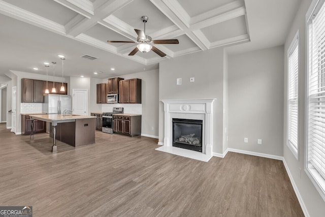 unfurnished living room featuring coffered ceiling, light wood-type flooring, a ceiling fan, baseboards, and a glass covered fireplace