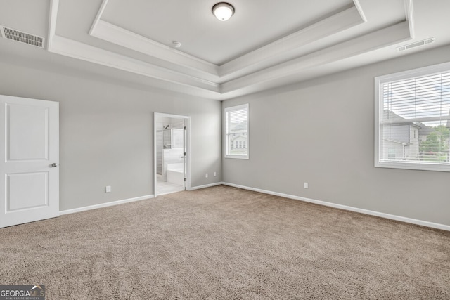 unfurnished bedroom with a tray ceiling, carpet flooring, crown molding, baseboards, and ensuite bath