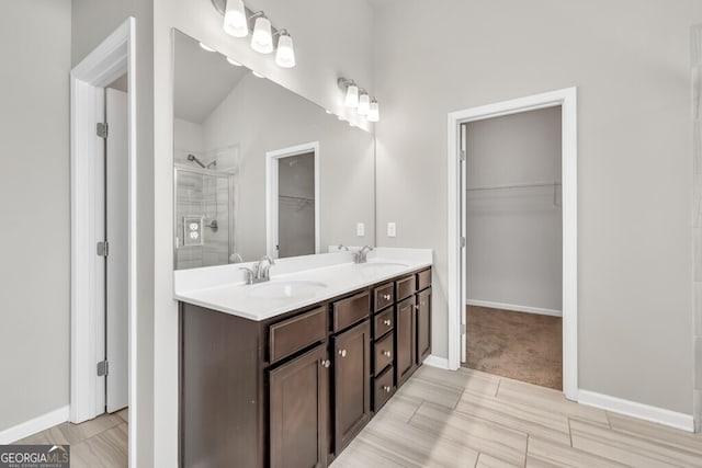 bathroom featuring a shower stall, a walk in closet, double vanity, and baseboards