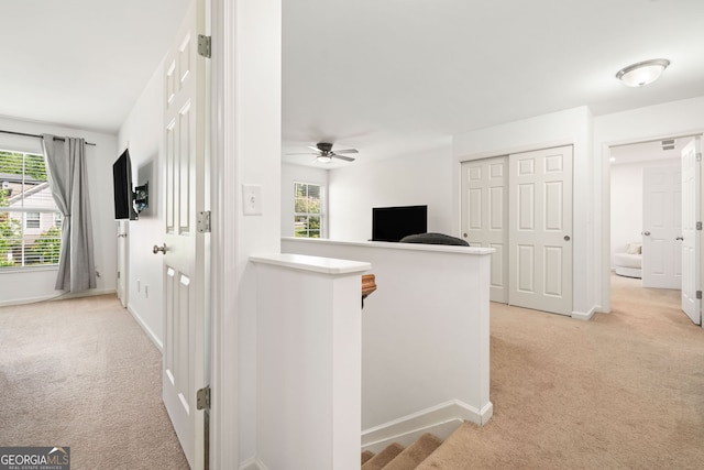 corridor featuring light carpet, plenty of natural light, and baseboards
