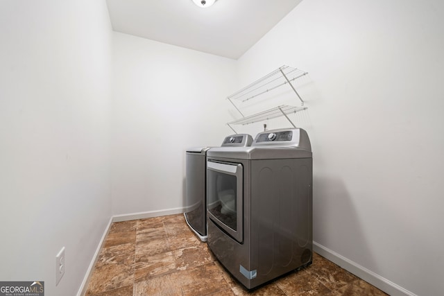 laundry area featuring washing machine and clothes dryer, baseboards, and stone finish floors