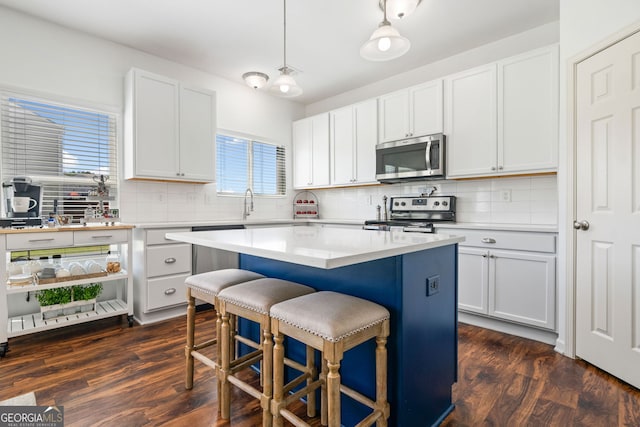 kitchen featuring appliances with stainless steel finishes, a breakfast bar, backsplash, a center island, and dark wood-type flooring