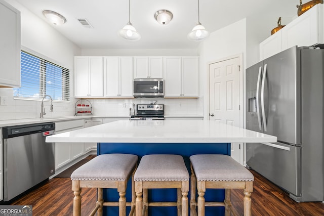 kitchen featuring appliances with stainless steel finishes, dark wood-type flooring, a breakfast bar area, backsplash, and white cabinetry