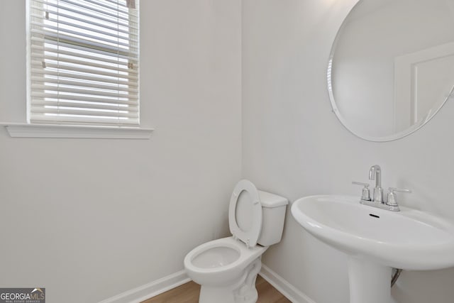 half bathroom featuring a sink, toilet, baseboards, and wood finished floors