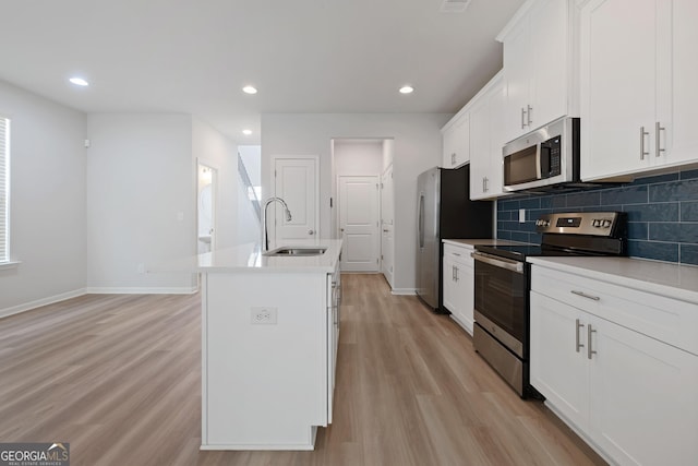kitchen featuring a sink, stainless steel appliances, a kitchen island with sink, baseboards, and light wood-style floors
