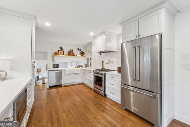 kitchen with high end appliances, custom range hood, white cabinetry, tasteful backsplash, and wood finished floors