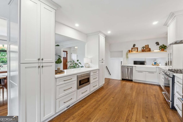 kitchen with appliances with stainless steel finishes, open shelves, light countertops, wood finished floors, and white cabinets