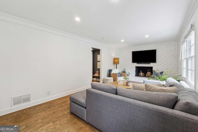 living room with wood finished floors, ornamental molding, recessed lighting, baseboards, and a brick fireplace