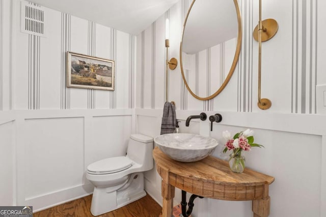 bathroom with toilet, wood finished floors, a sink, and wallpapered walls