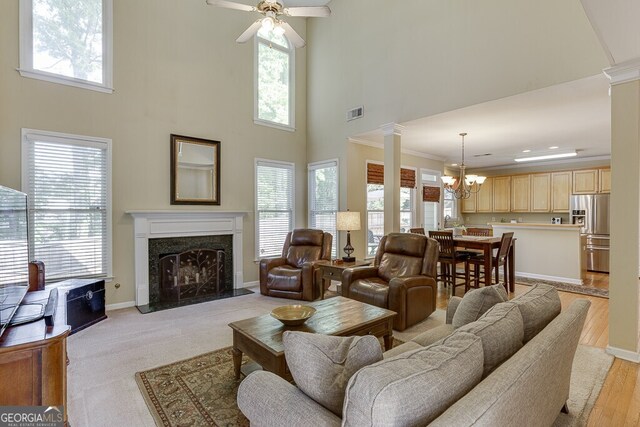 living area featuring ceiling fan with notable chandelier, a high ceiling, ornate columns, ornamental molding, and a high end fireplace
