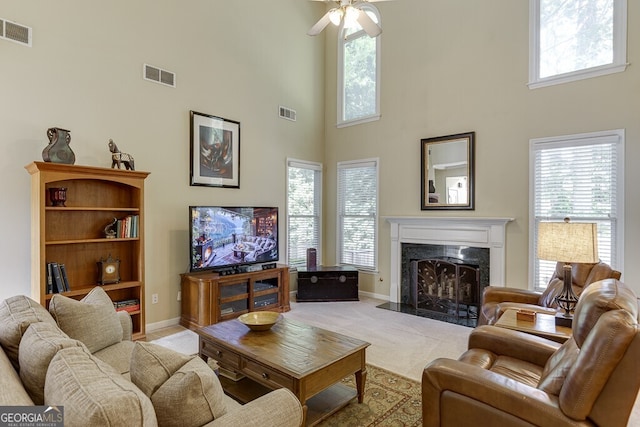 living area featuring a healthy amount of sunlight, visible vents, a high ceiling, and a high end fireplace