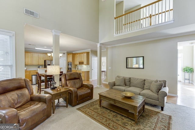 living area featuring a towering ceiling, visible vents, decorative columns, and light carpet