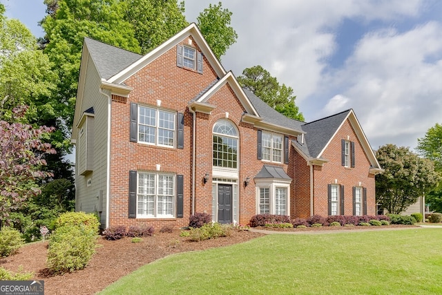 colonial house with roof with shingles, brick siding, and a front yard