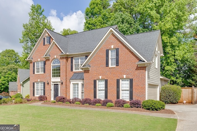colonial home featuring fence, brick siding, driveway, a front lawn, and a shingled roof