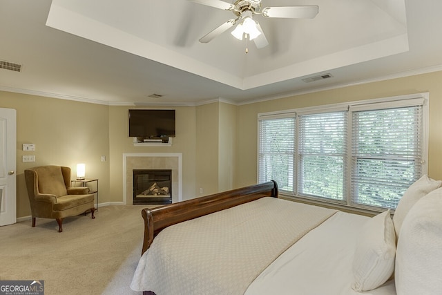 bedroom with a tray ceiling, visible vents, a tile fireplace, and light carpet