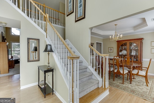 staircase featuring baseboards, a chandelier, crown molding, wood finished floors, and a high ceiling