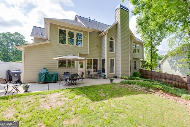 back of property with a yard, a patio area, a chimney, and fence
