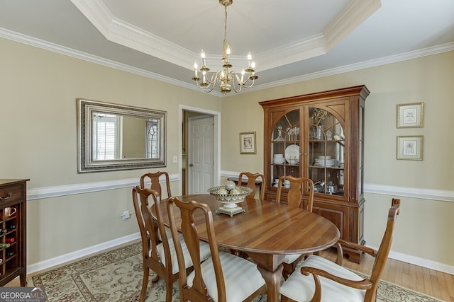 dining space with a tray ceiling, an inviting chandelier, ornamental molding, and light wood-type flooring