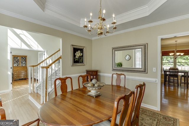 dining space with light wood finished floors, a tray ceiling, crown molding, a chandelier, and stairs