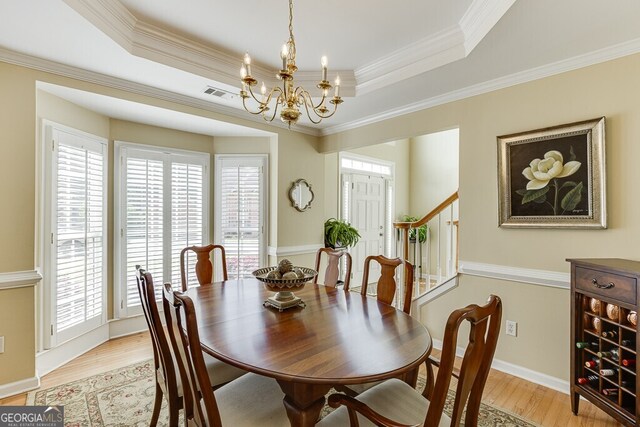 dining room with a chandelier, a raised ceiling, light wood finished floors, and ornamental molding