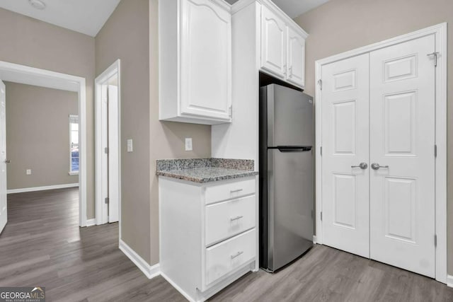 kitchen featuring freestanding refrigerator, light stone counters, white cabinets, and light wood-type flooring