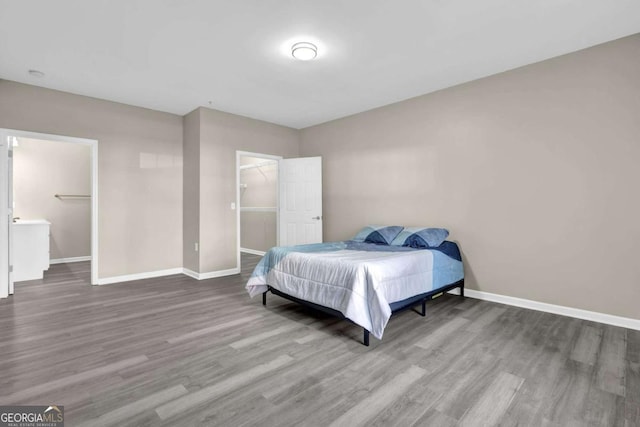 bedroom featuring a spacious closet, baseboards, a closet, and wood finished floors