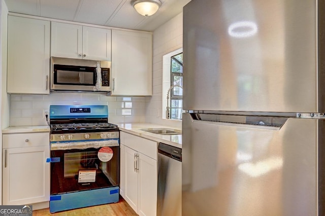 kitchen featuring light wood-type flooring, decorative backsplash, light countertops, white cabinets, and appliances with stainless steel finishes