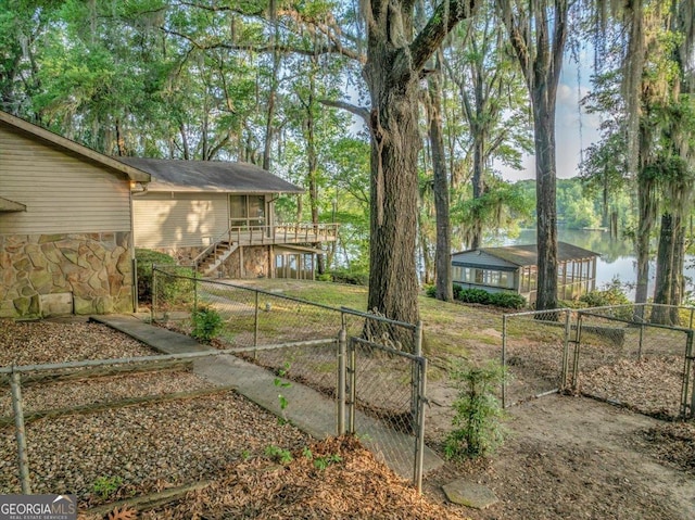 view of yard featuring a gate, a deck with water view, a fenced backyard, and stairs