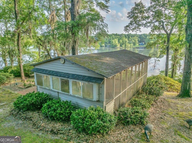 view of property exterior with a water view, a sunroom, a shingled roof, and fence