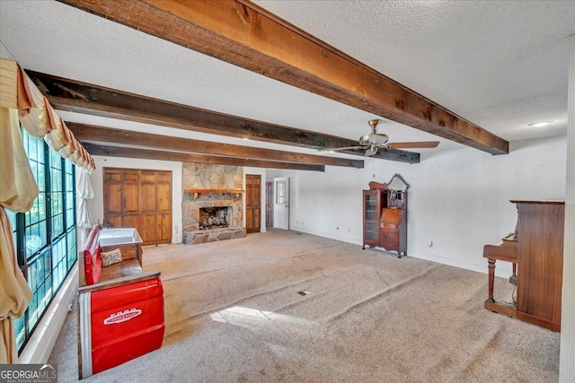 unfurnished living room with beam ceiling, a fireplace, carpet floors, a ceiling fan, and baseboards