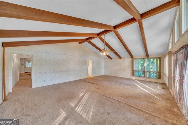 unfurnished living room with wallpapered walls, plenty of natural light, lofted ceiling with beams, and carpet floors