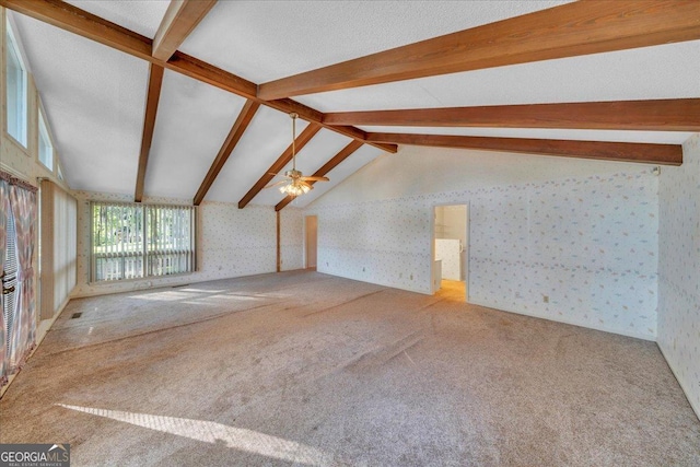 unfurnished living room with ceiling fan, vaulted ceiling with beams, wallpapered walls, and carpet