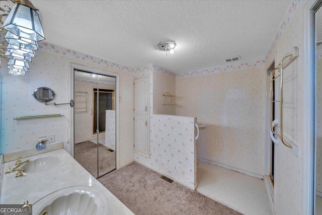 bathroom with wallpapered walls, a textured ceiling, visible vents, and a sink