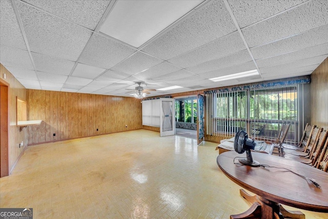 interior space featuring a paneled ceiling, wooden walls, and ceiling fan