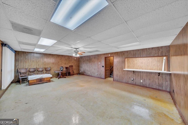 unfurnished room featuring a drop ceiling, wood walls, and ceiling fan