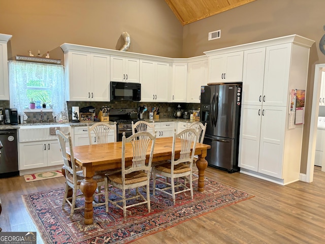 kitchen with visible vents, a sink, high vaulted ceiling, wood finished floors, and black appliances