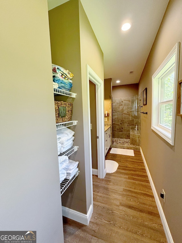 bathroom featuring a tile shower, baseboards, vanity, and wood finished floors
