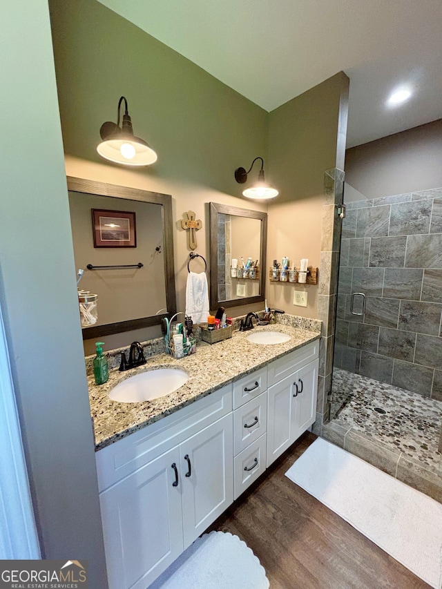 full bath with double vanity, wood finished floors, a tile shower, and a sink