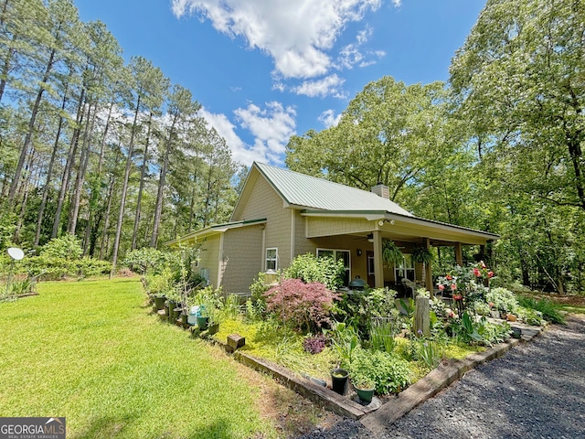 view of home's exterior featuring a yard, a chimney, metal roof, and ceiling fan