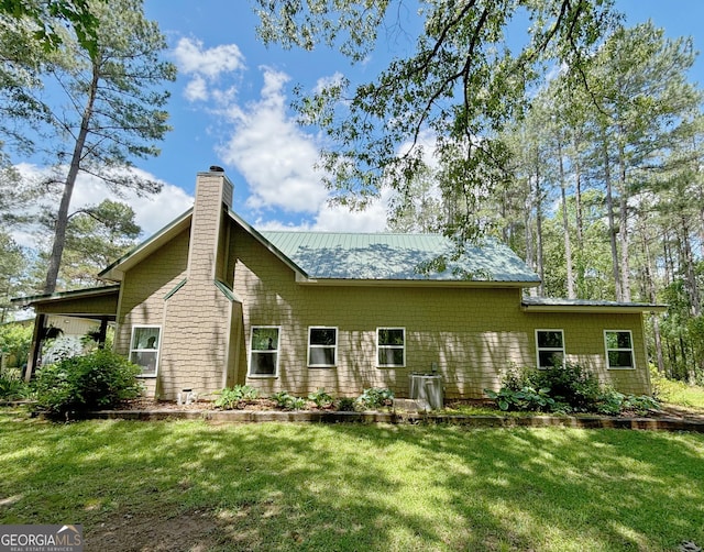 rear view of property featuring a yard, a chimney, and metal roof