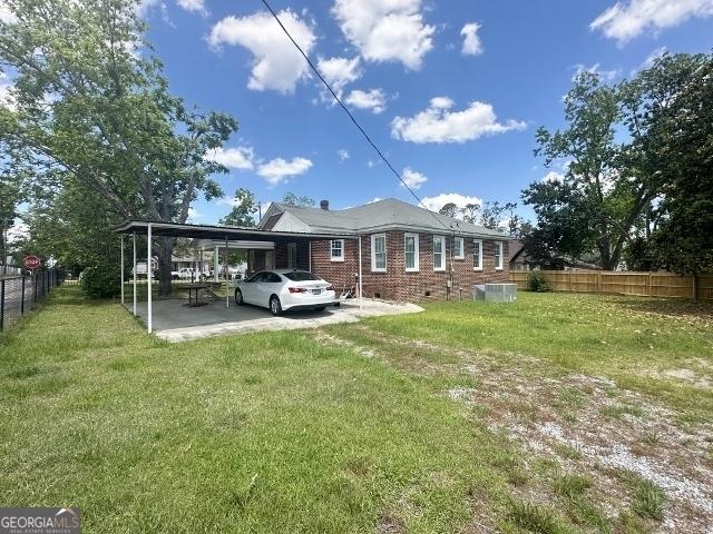 327 W Church St, Swainsboro, GA 30401 - back of house featuring brick siding, fence, a lawn, and a carport