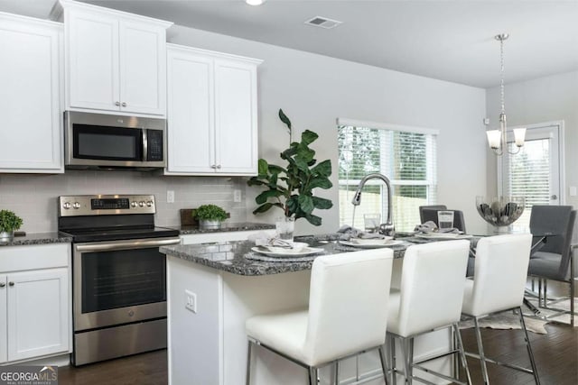 kitchen featuring stainless steel appliances, dark wood-type flooring, visible vents, an island with sink, and decorative backsplash